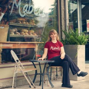 A picture of the founder of Mabel's bakery, Lorraine Hawley sitting outside Mabel's store